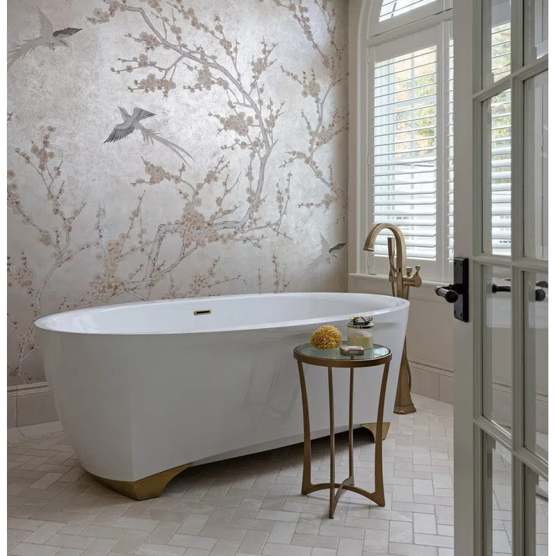 Elegant bathroom featuring a white freestanding tub, gold fixtures, floral wallpaper, and arched window with shutters.