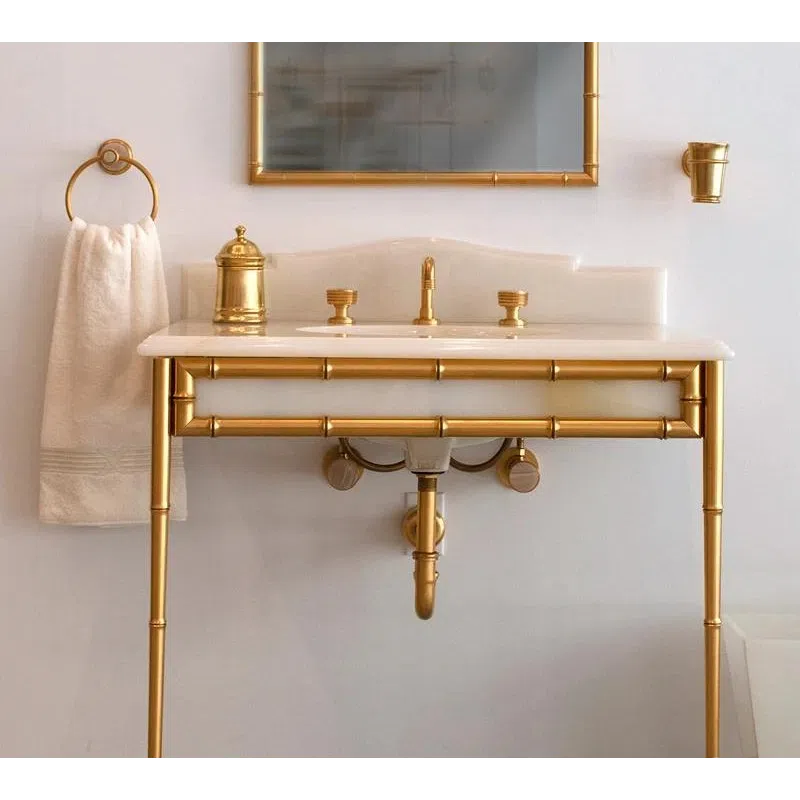 Elegant bathroom sink with gold metal frame, matching gold faucet fixtures, mirror, and towel holder.