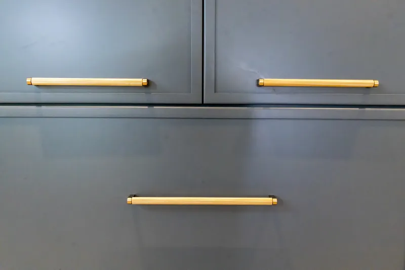 Close-up of modern gray cabinet drawers with brass handles.
