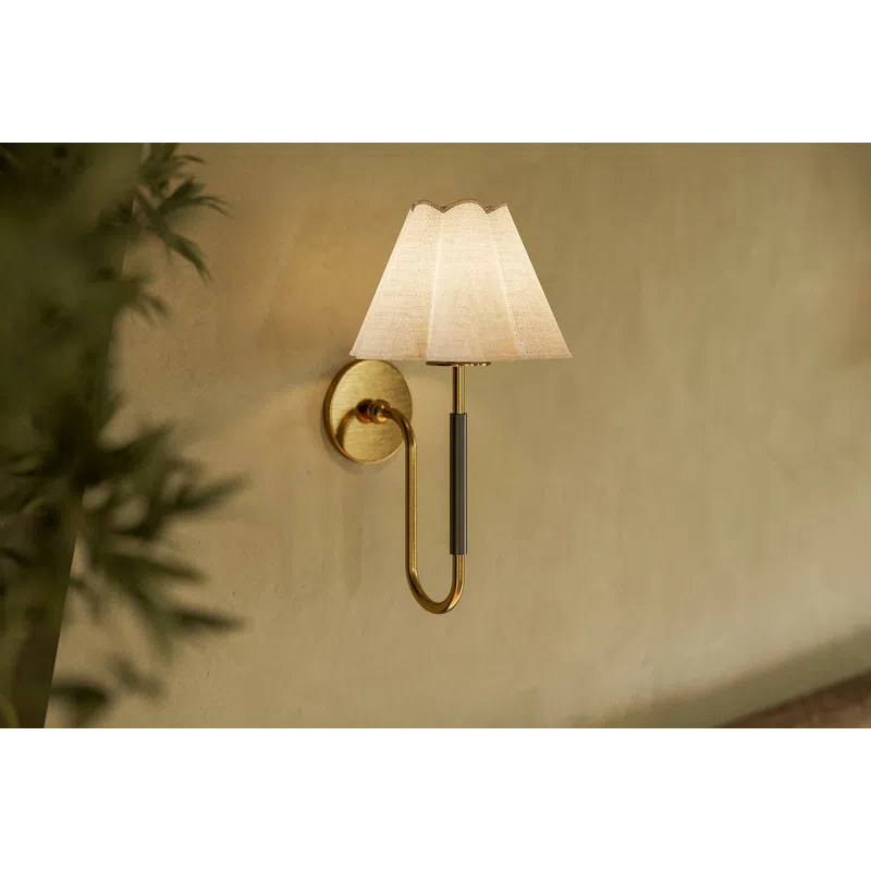 Elegant wall sconce with brass arm and white fabric shade mounted on a beige textured wall.