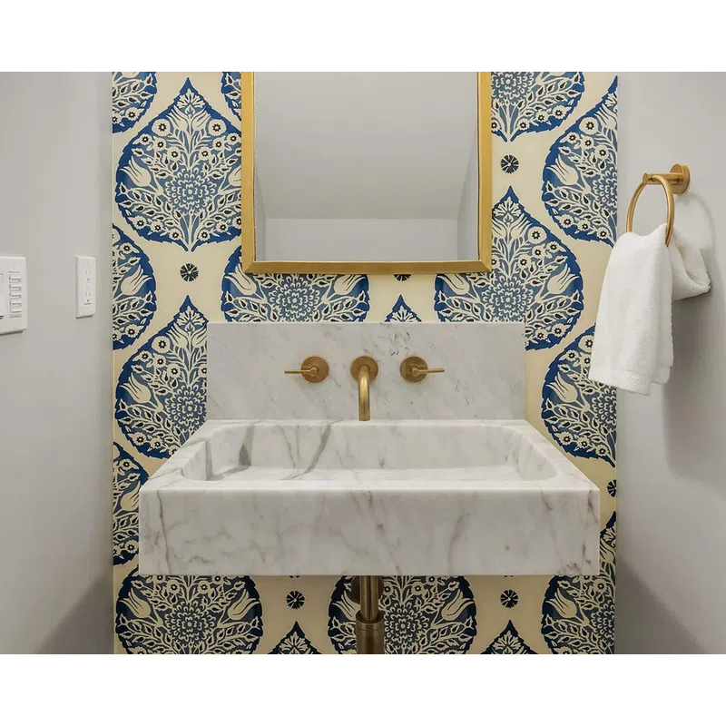 Marble sink with gold fixtures, ornate gold-framed mirror, blue and white patterned wallpaper, and gold wall sconces.