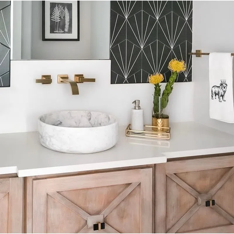 Modern bathroom vanity with a round marble sink, gold faucet, geometric black wall art, and wooden cabinets