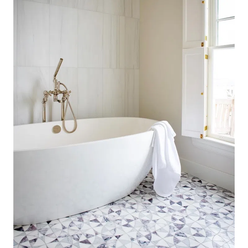 Modern white freestanding bathtub with chrome faucet and white towel beside window on patterned tile floor.