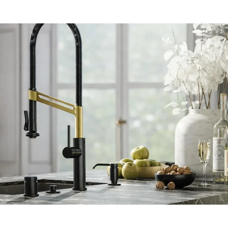 Modern kitchen faucet with black and brass finish on marble countertop near bowl of walnuts and green apples.