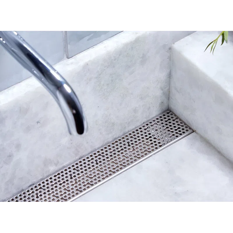 Close-up of modern chrome faucet and wall-mounted handle over white marble sink with metal drain cover.