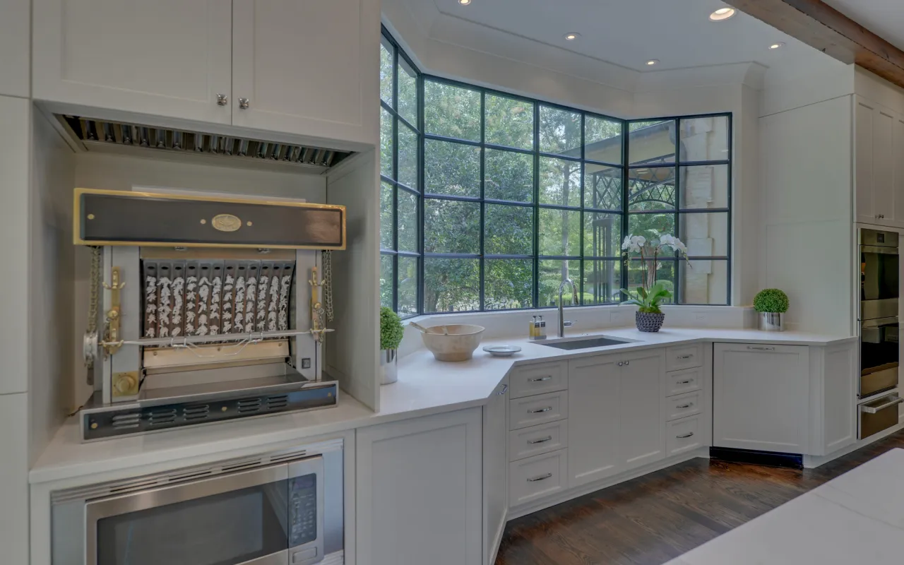 Modern kitchen with white cabinetry, large black-framed windows, built-in appliances, and an automatic rotisserie oven.