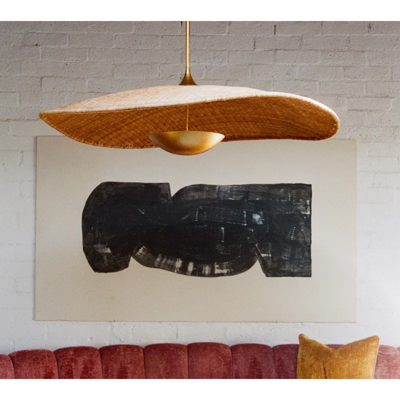Curved red velvet sofa with mustard pillow under large abstract black art and woven pendant light.