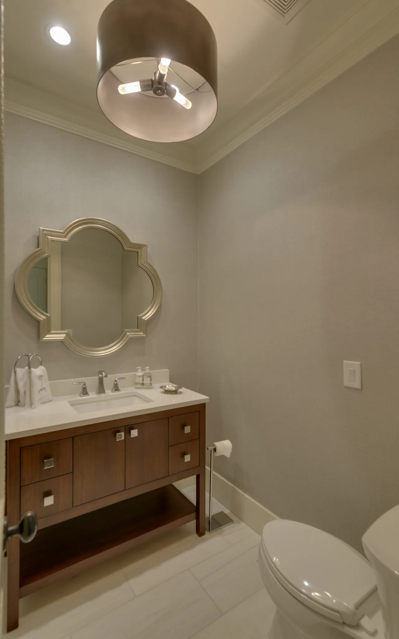 Modern bathroom with wooden vanity, decorative mirror, toilet, and overhead light fixture in neutral tones