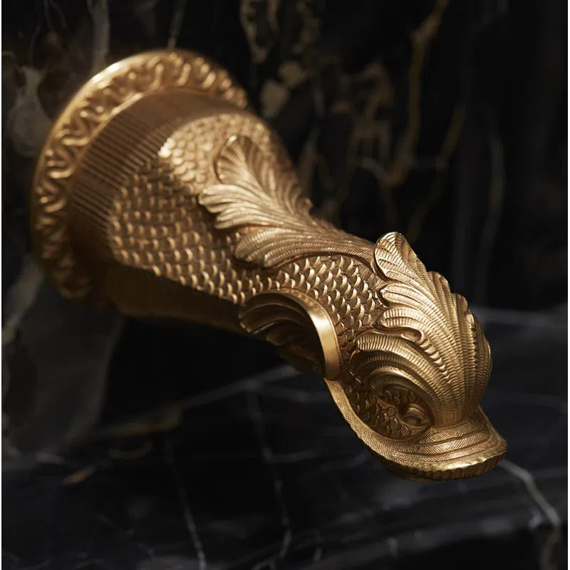 Ornate gold fish-shaped faucet on black marble with intricate scales and leaf designs in luxury bathroom.