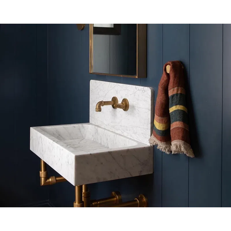 Modern bathroom with white marble sink, brass fixtures, arched mirror, navy blue walls, and striped hanging towel.
