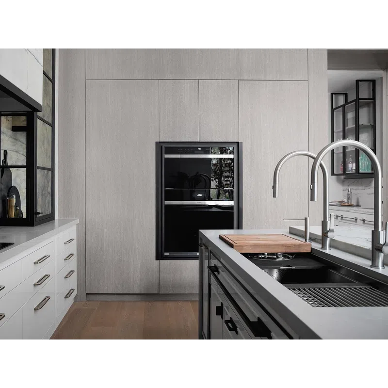 Modern kitchen with sleek white cabinets, built-in oven, black countertop, and dual curved faucets on island sink.