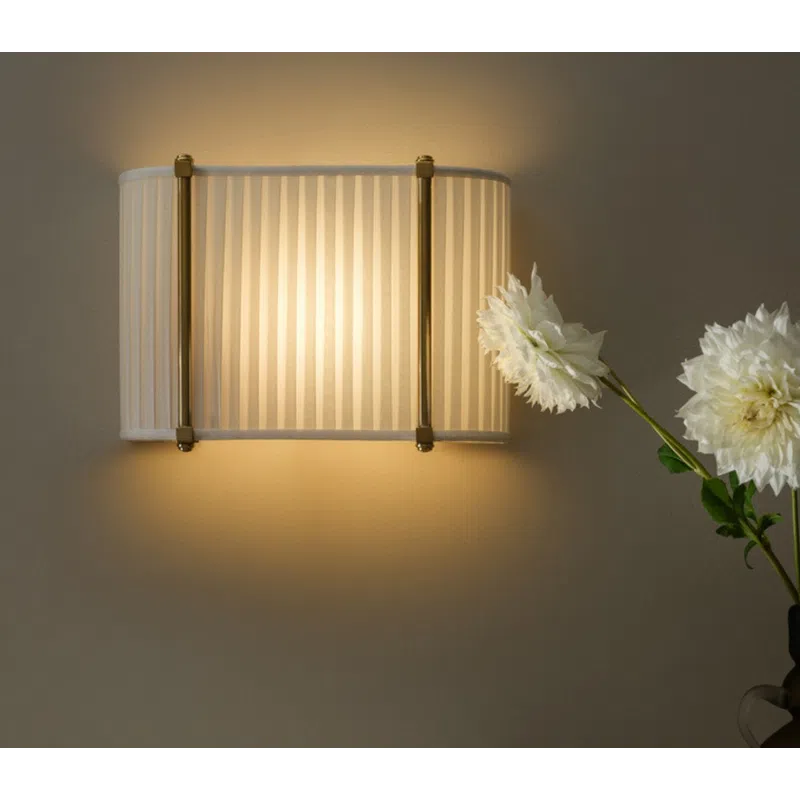 Warm light from a striped wall sconce illuminates a decorative marble mantel with white flowers and a dark vase.