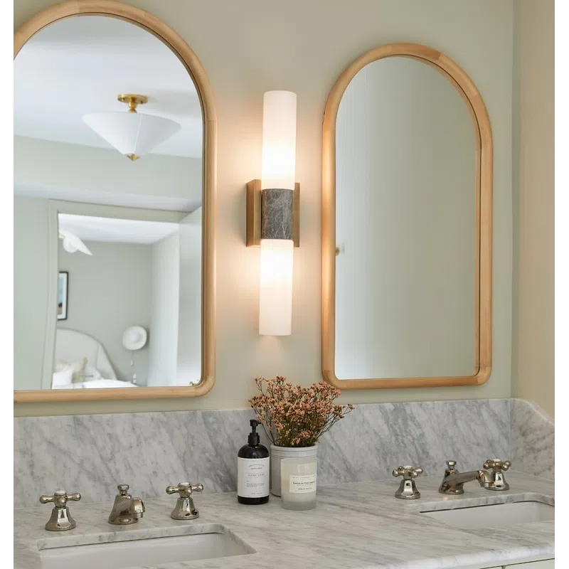 Modern bathroom vanity with marble countertop, double sinks, brass fixtures, arched mirrors, and wall sconce lighting.