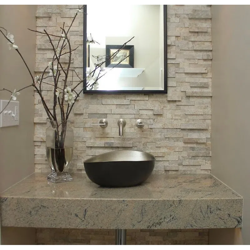 Modern bathroom sink area with stone wall, black vessel sink, rectangular mirror, and decorative vase with branches.