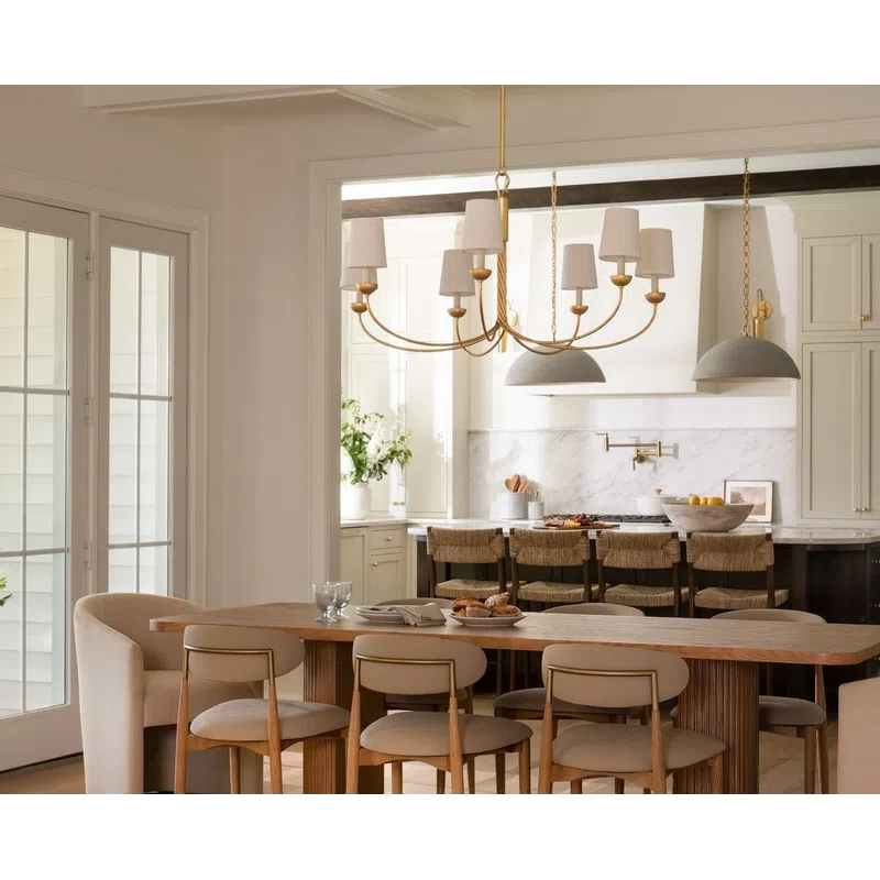Modern dining room with wooden table, beige chairs, gold chandelier, and open kitchen with bar stools.