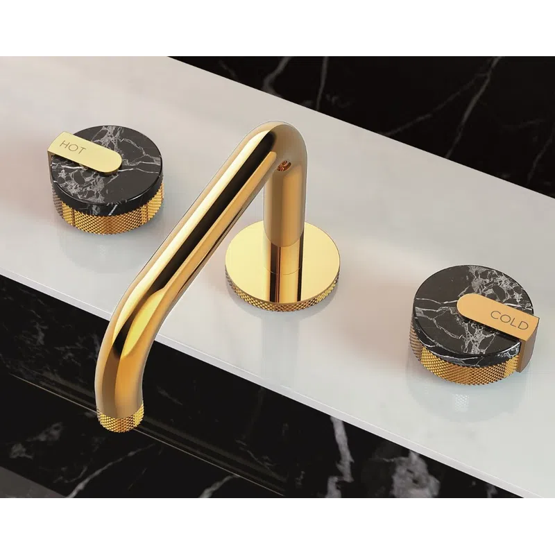 Modern gold faucet with black marble hot and cold knobs on a white countertop and black marble surroundings.