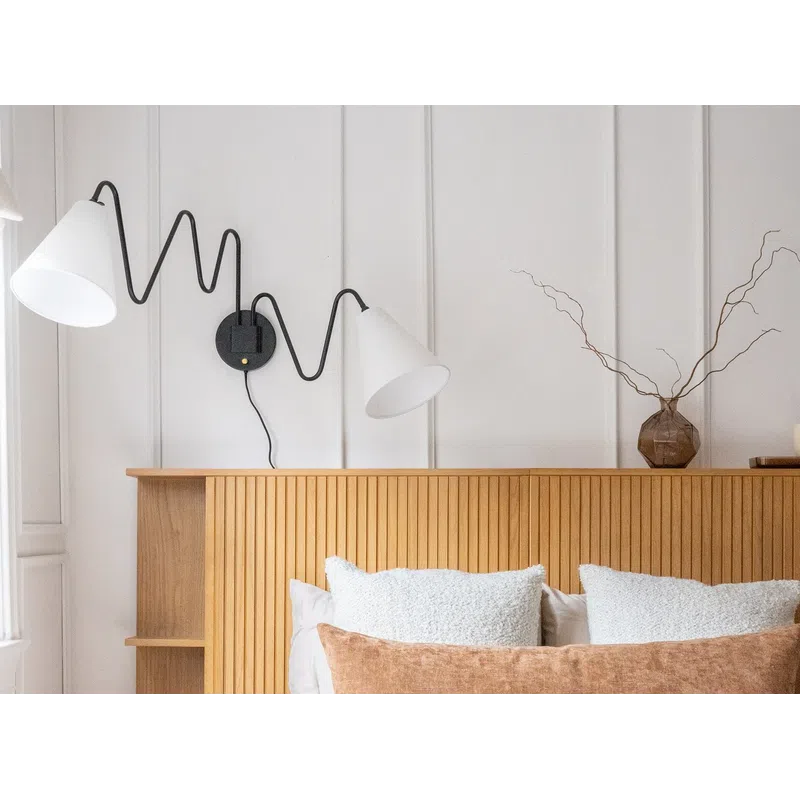 Cozy modern bedroom with wooden headboard, white bedding, textured pillows, wall-mounted zigzag lamp, and decorative vase.