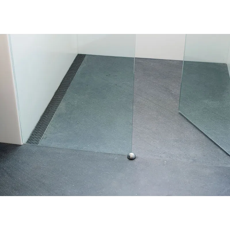 Modern minimalistic shower area with gray stone floor, glass partitions, and a metal drain along the corner.