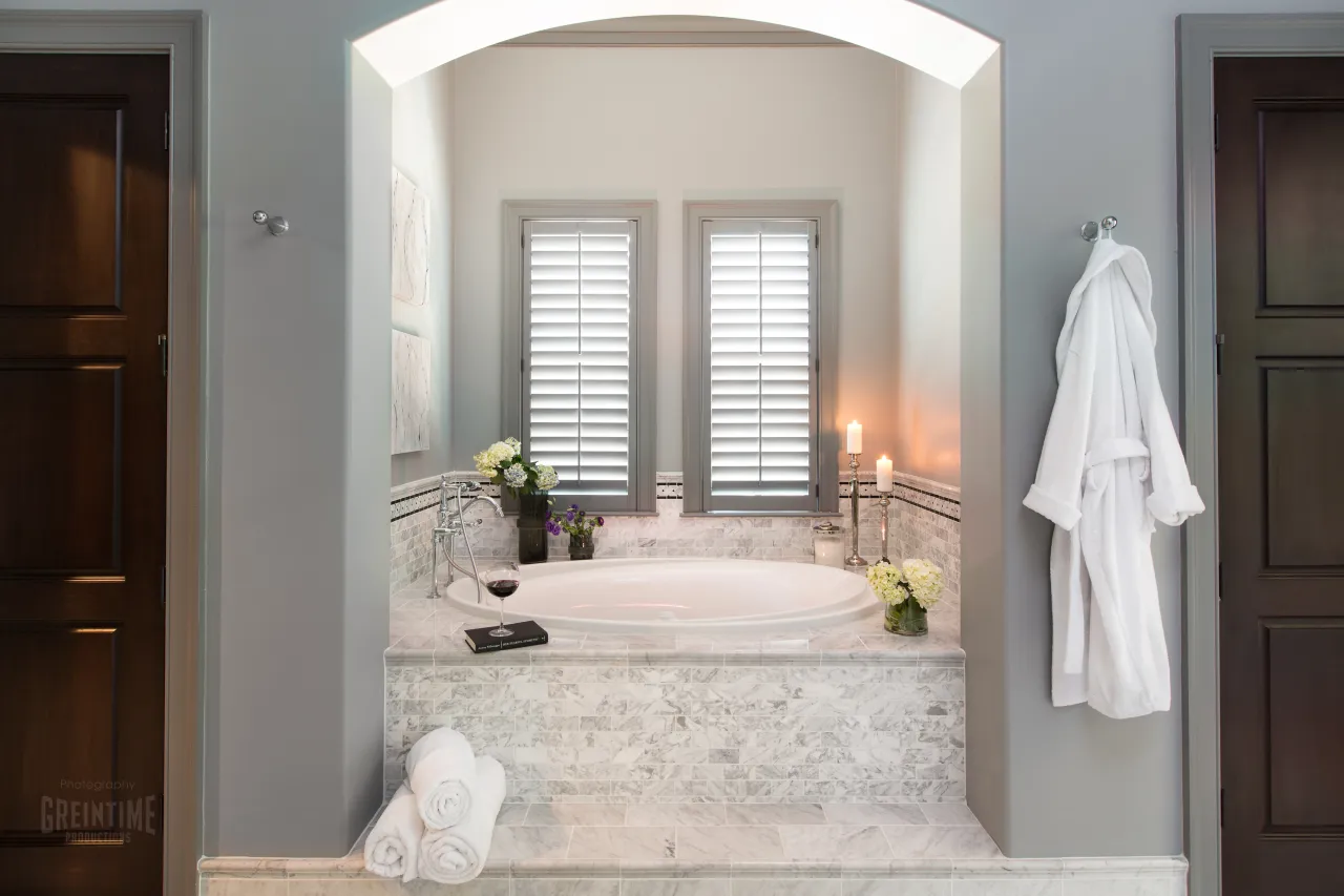 Luxurious marble bathtub with candles, flowers, white towels, and a bathrobe in a modern bathroom setting