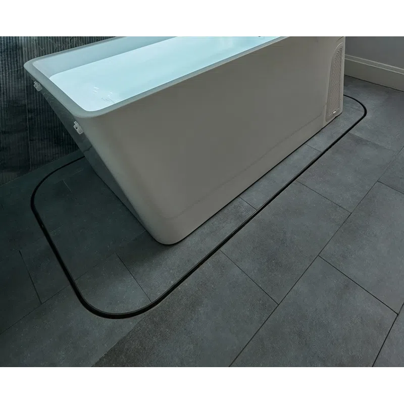 Modern rectangular white bathtub filled with water against a textured gray tiled wall and floor.