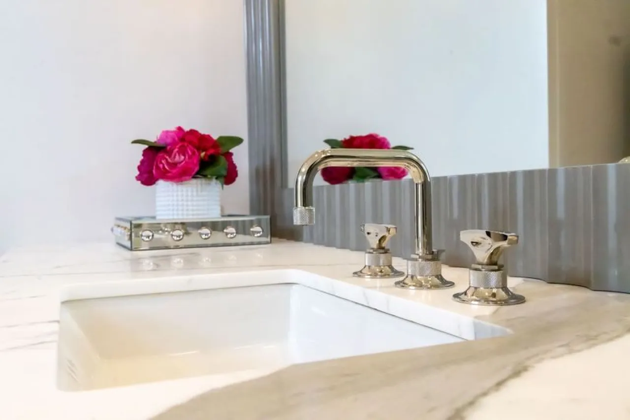 Modern bathroom sink with chrome faucet and vibrant pink flowers on marble countertop below a large mirror.