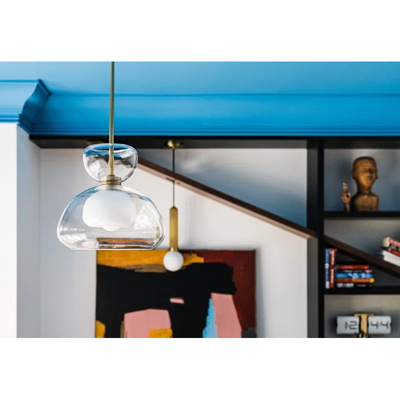 Modern pendant light hangs in front of abstract painting and bookshelf with decorative items in stylish room.