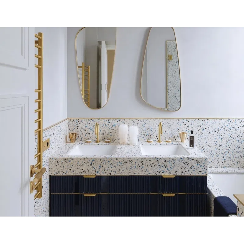 Modern bathroom with terrazzo double sink, gold fixtures, navy cabinets, two asymmetrical mirrors, and white wall lights.