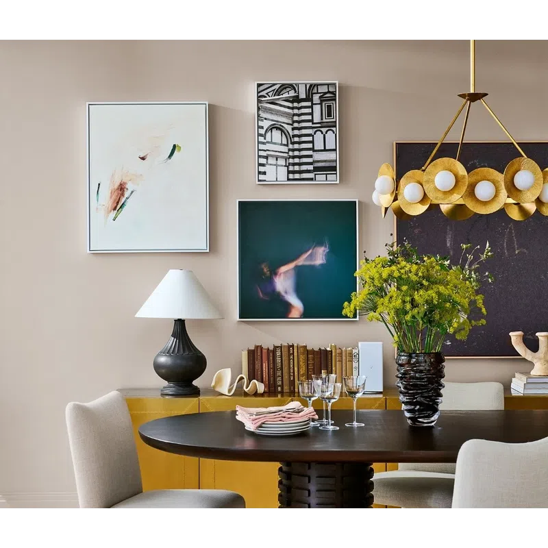 Modern dining room with round dark wood table, beige chairs, yellow sideboard, abstract art, and floral centerpiece.