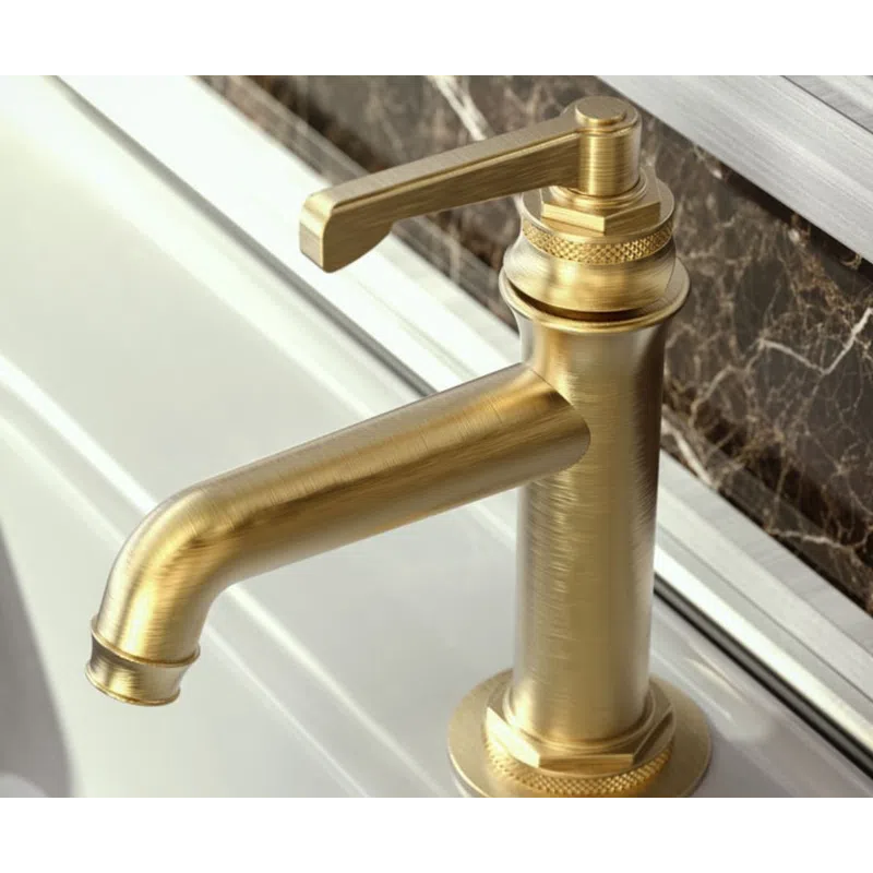 Brushed gold modern faucet mounted on white sink with dark marble backsplash in bathroom.