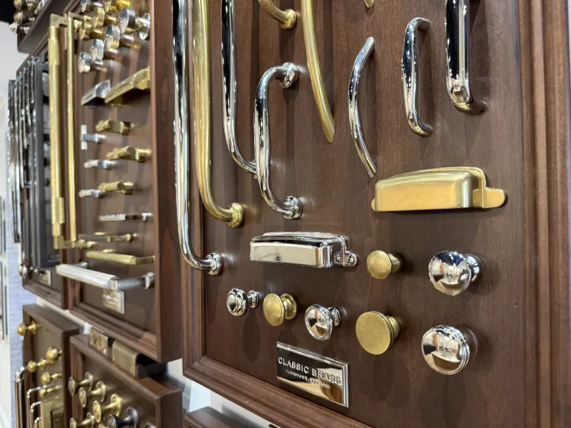 Various brass and chrome cabinet handles and knobs displayed on wooden boards in a showroom.