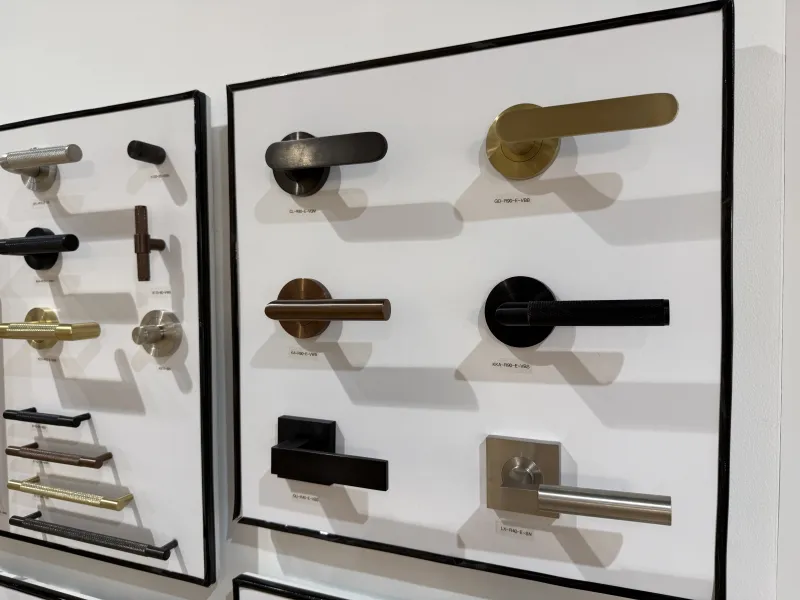 Display of various modern door handles in different finishes mounted on white boards against a wall.