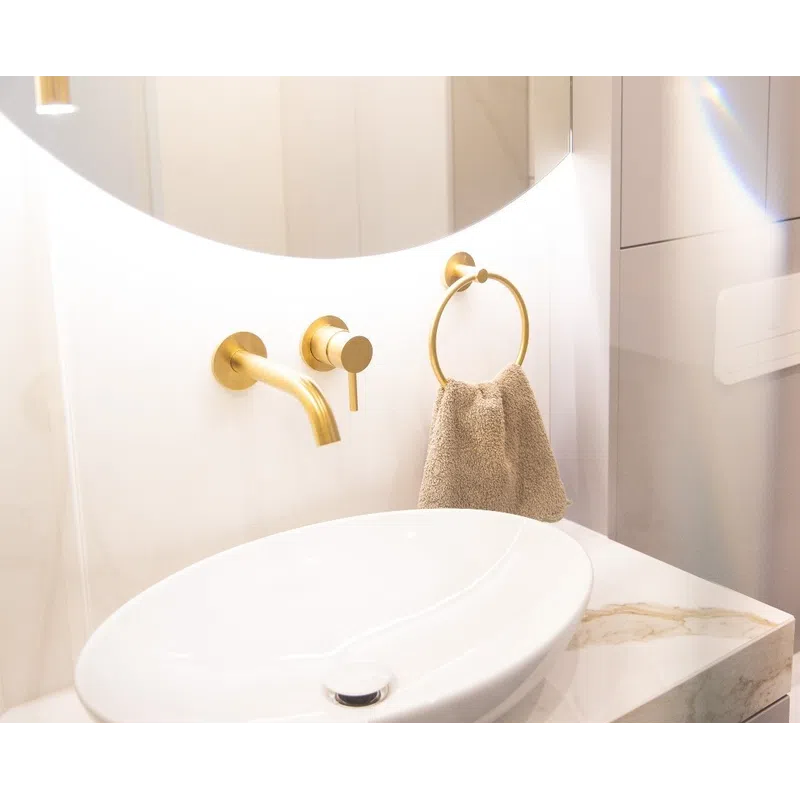 Modern bathroom sink with gold faucet and towel ring, illuminated white countertop and round mirror.