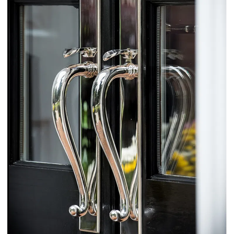 Close-up of shiny silver door handles on black-framed glass doors with reflections.