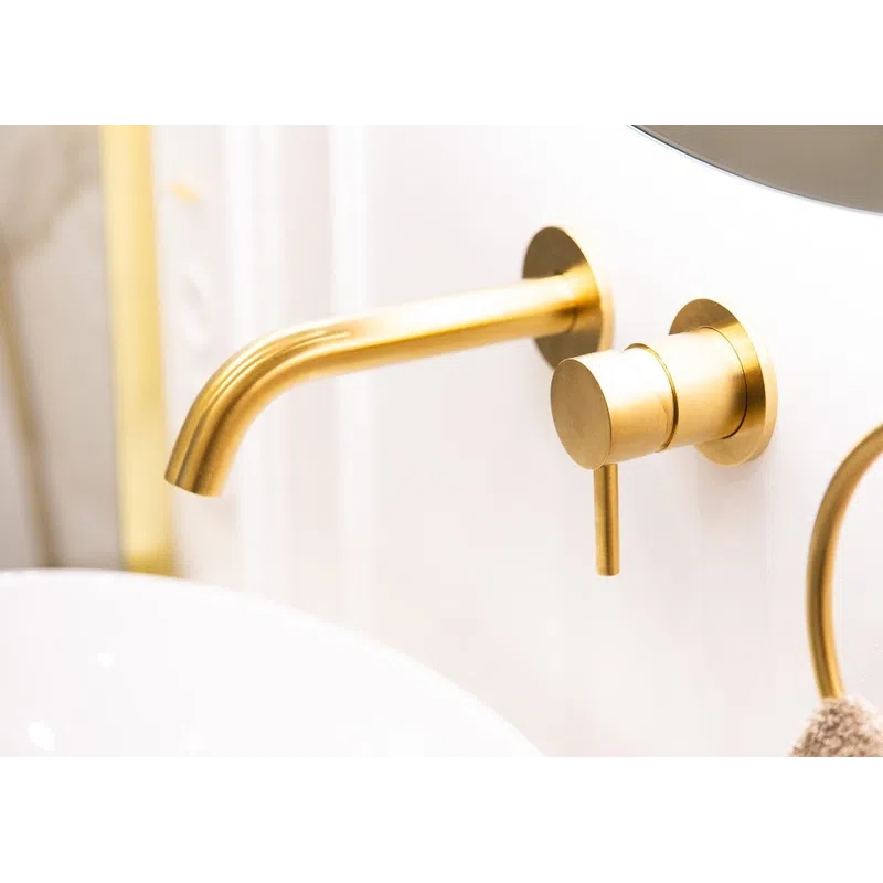 Modern bathroom faucet with gold finish mounted on white wall above white sink basin and beige towel.