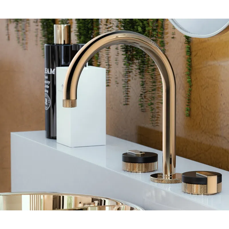 Modern gold faucet and matching basin with black and gold handles on white countertop with green plants background