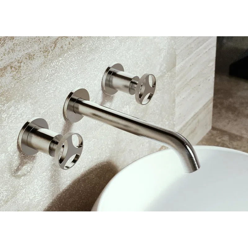 Modern stainless steel wall-mounted faucet with two handles above a round white sink on textured stone wall.