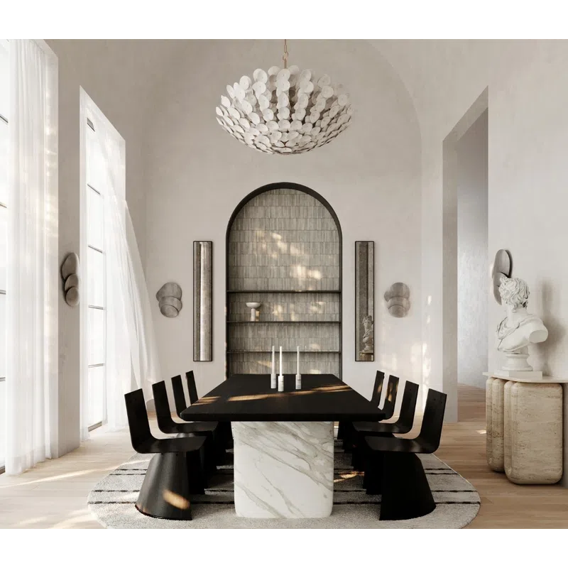 Modern dining room with black chairs, marble table base, round rug, large chandelier, and bright natural light.