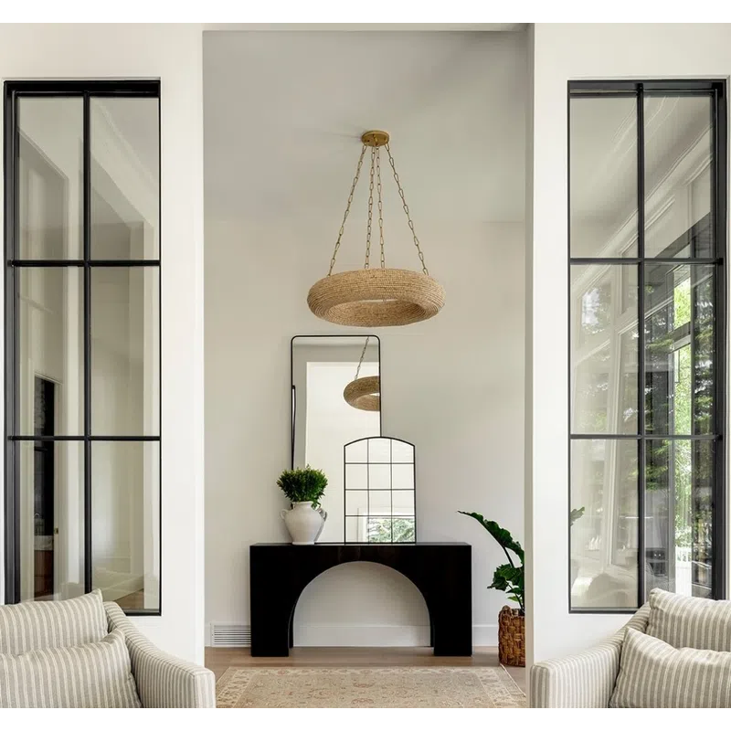 Bright living space with striped armchairs, black console table, mirrors, plants, and woven ceiling light.