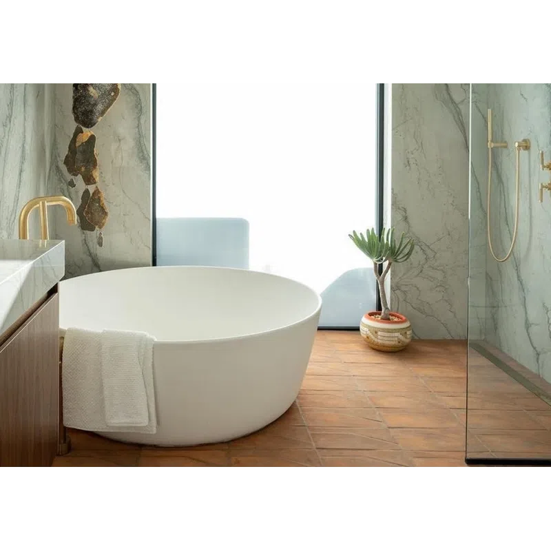 Modern bathroom with a round white bathtub, marble walls, wooden floor, glass shower, and decorative plant.