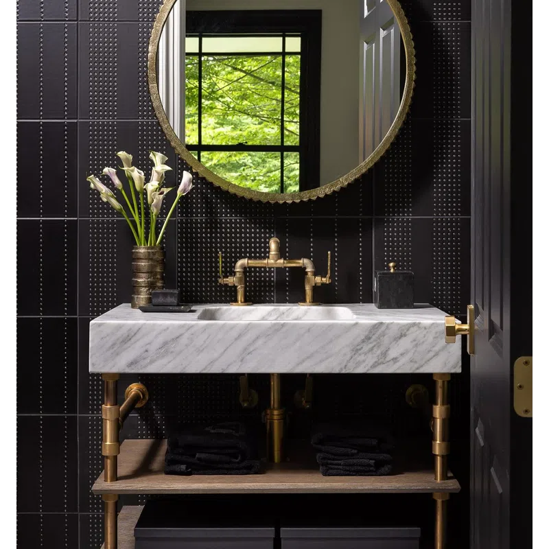 Modern bathroom with black tiled walls, round gold mirror, white marble sink, gold fixtures, and fresh flowers.