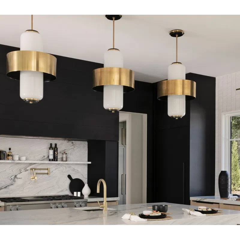 Modern kitchen with black walls, marble island, gold fixtures, and black velvet chairs under brass pendant lights.