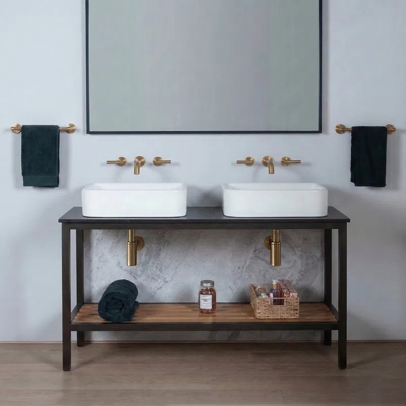 Modern double bathroom sinks with gold faucets, black towels, and wooden shelf with toiletries underneath.