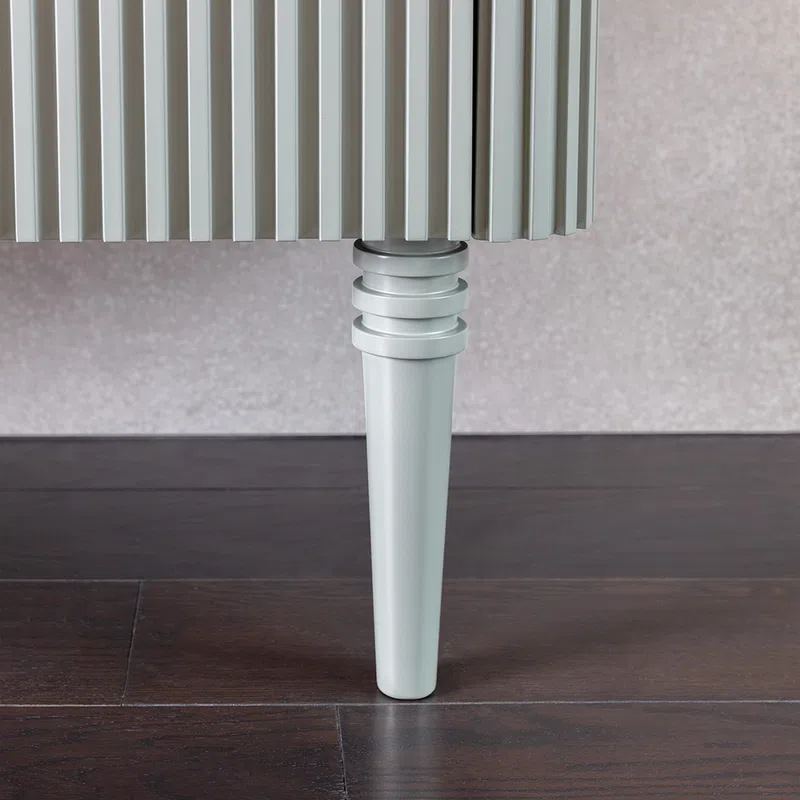Close-up of a white wooden tapered leg supporting a piece of ribbed furniture on dark hardwood flooring.