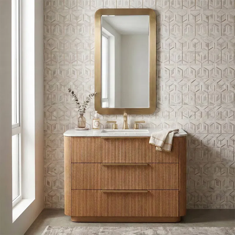 Modern bathroom vanity with wooden slatted drawers, brass faucet, large rounded rectangular mirror, and geometric tile wall.