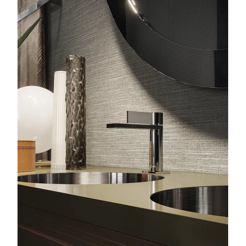 Modern bathroom countertop with dual round sinks, sleek chrome faucet, decorative vases, and textured wall.