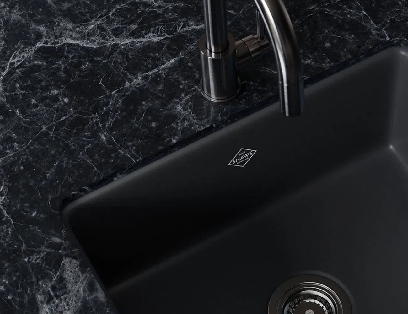 Modern black kitchen sink with stainless steel faucet installed in a dark marble countertop