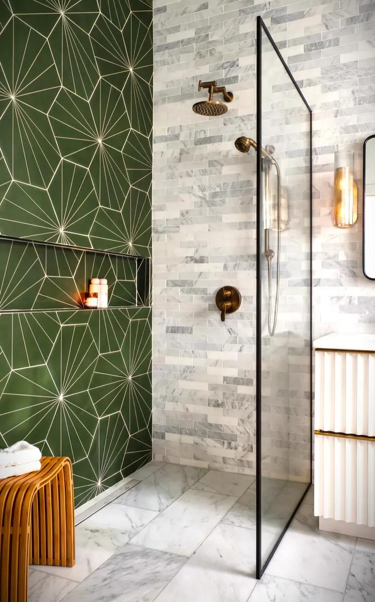 Modern bathroom shower with green geometric wall tiles, brass fixtures, glass partition, and marble flooring.