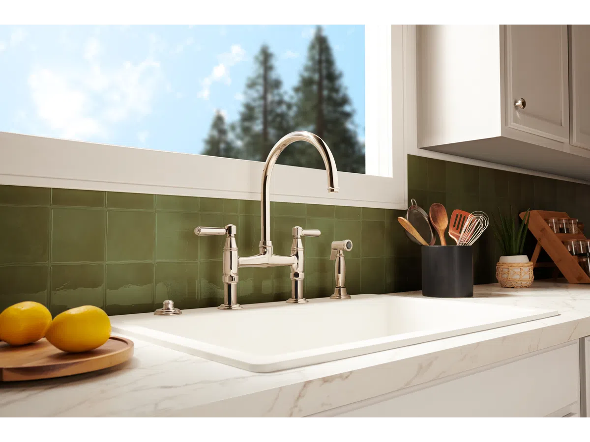 Modern kitchen sink with polished chrome faucet, green tile backsplash, and utensils in a black holder.