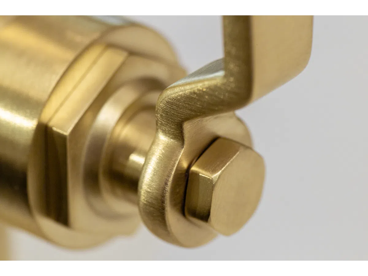 Close-up of a brass hex bolt and wrench on a mechanical component with a blurred background.