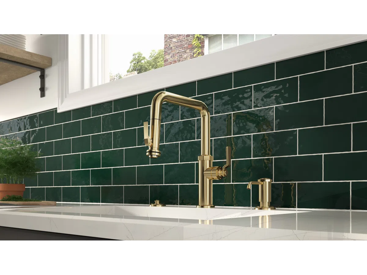 Modern kitchen sink with brass faucet and deep green subway tile backsplash under a large window.